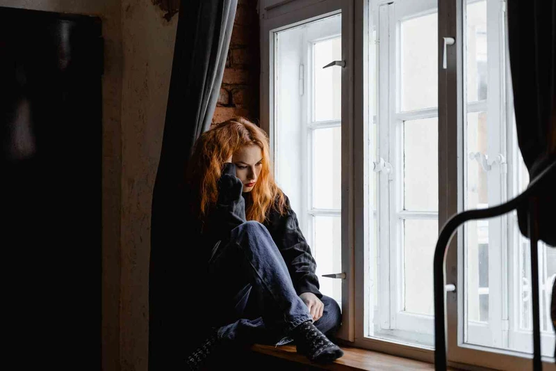 Junge Frau sitz vor dem Fenster und guckt ersch&ouml;pft